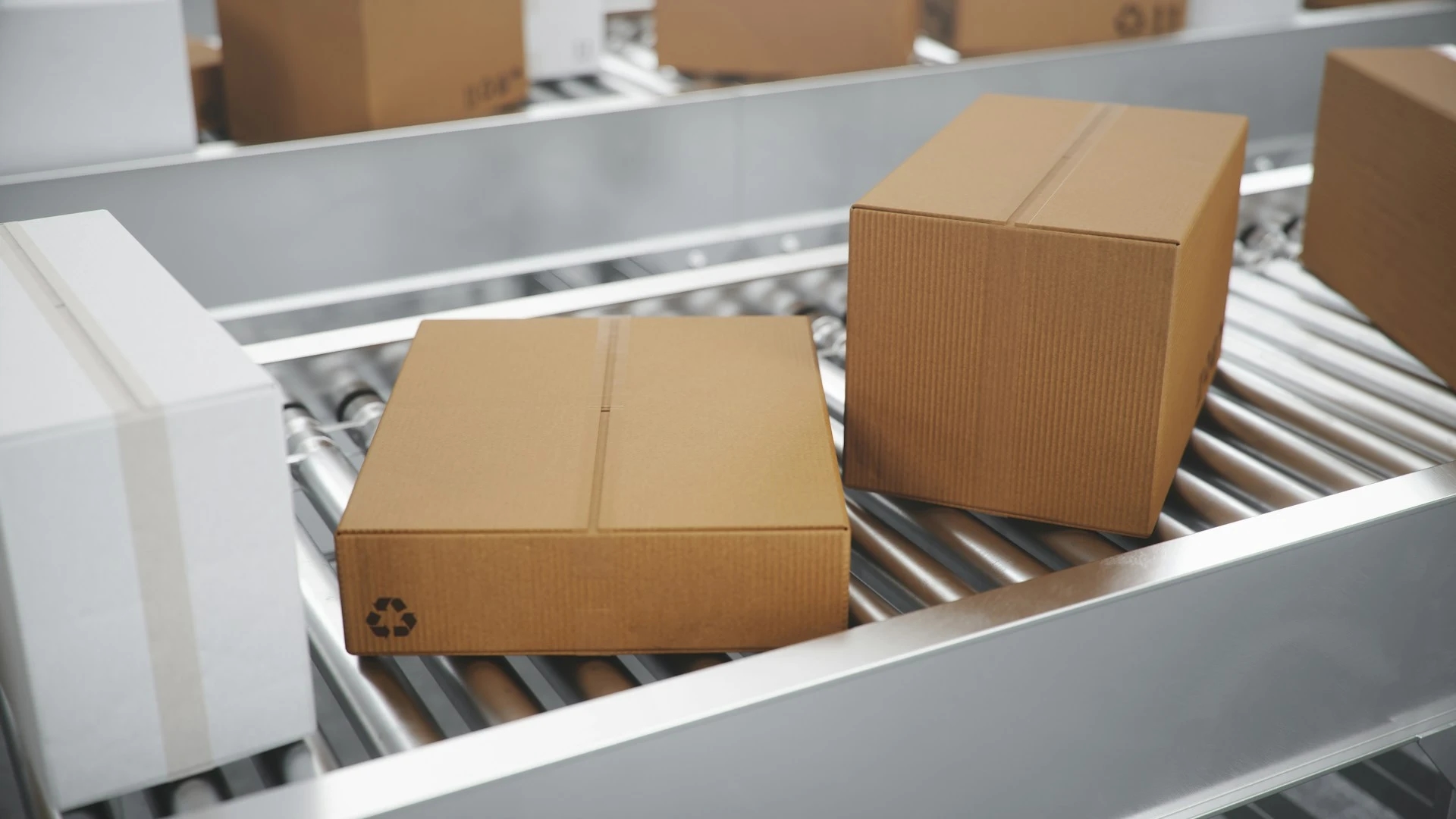 Two cardboard boxes on a metal conveyor belt, with one box displaying a recycling symbol, surrounded by other moving packages.