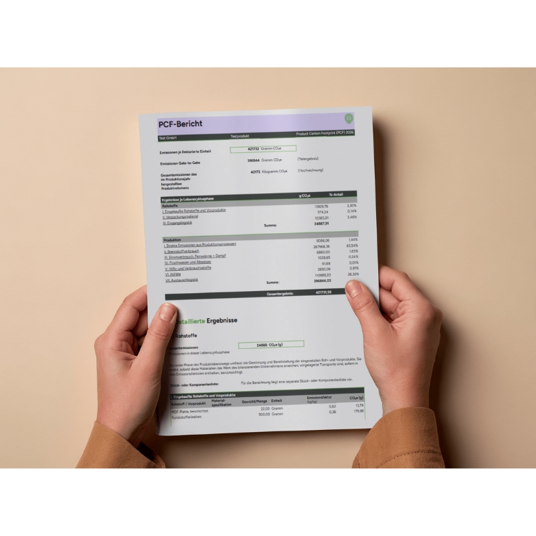 Hands holding a printed report titled "PCF-Bericht" with tables and data, on a beige background.