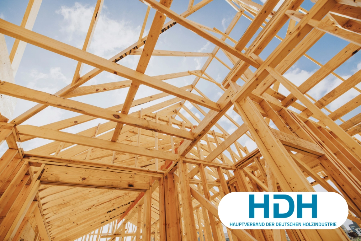 Wooden framework of a building under construction, set against a blue sky. HDH logo in the corner.